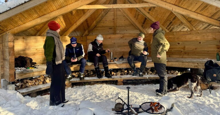 Ihmiset hyväntuulisena viettämässä talvipäivää laavulla.