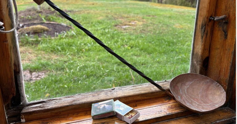 kuvassa saunan ikkuna, jossa ikkunalaudalla on löylykauha ja tulitikut. Ikkunasta näkyy pihapiiri. Sauna on pihasauna.